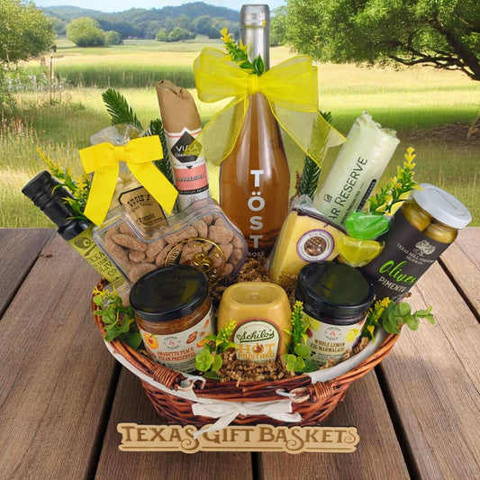 a celebration themed Texas Gift Basket, filled with pecans, non alcoholic rose, olives, crackers, olive oil, mustard, marmalade, yogurt pretzels, crackers, and sausage, in a lined willow basket with prairie background