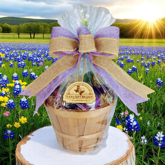 A Texas gift basket containing various spa products, including a Texas Bluebonnet candle, wrapped in a transparent bow with purple accents, set against a field of bluebonnets.