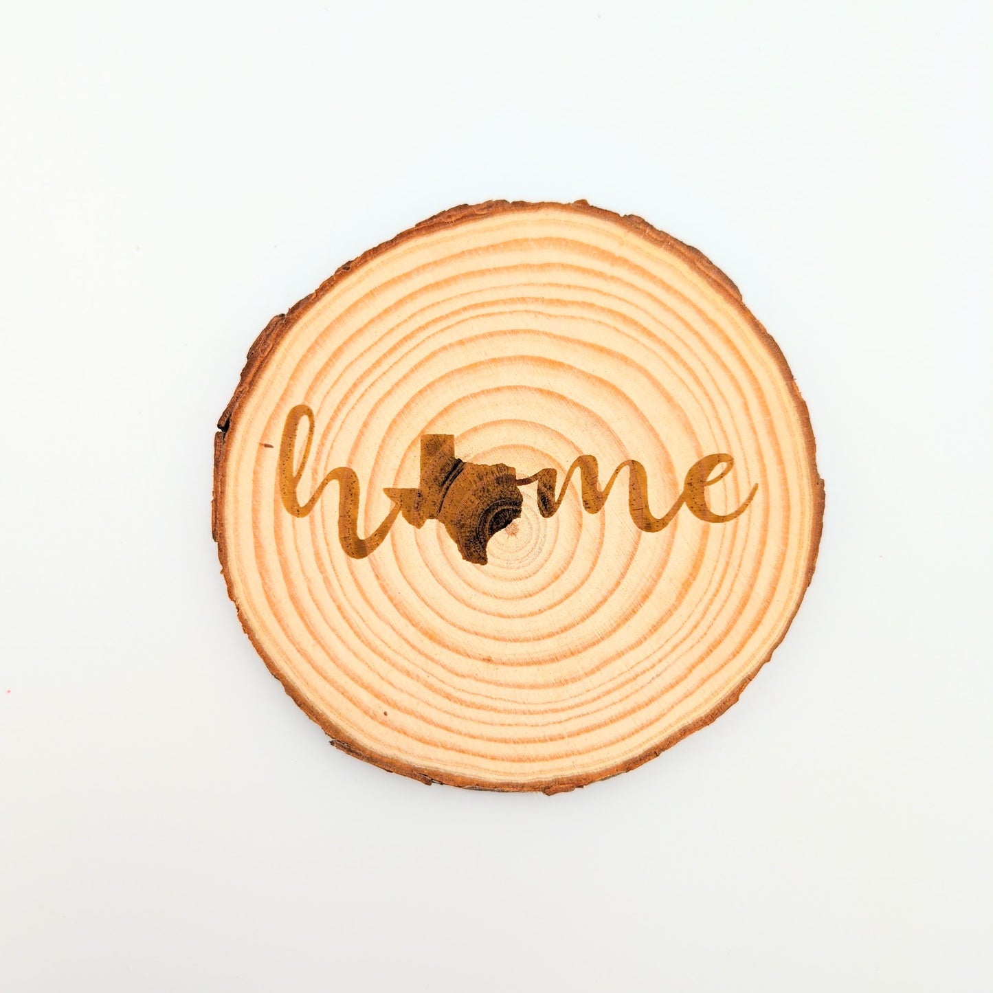 a wood slice coaster with engraving in cursive of the word home with the image of texas