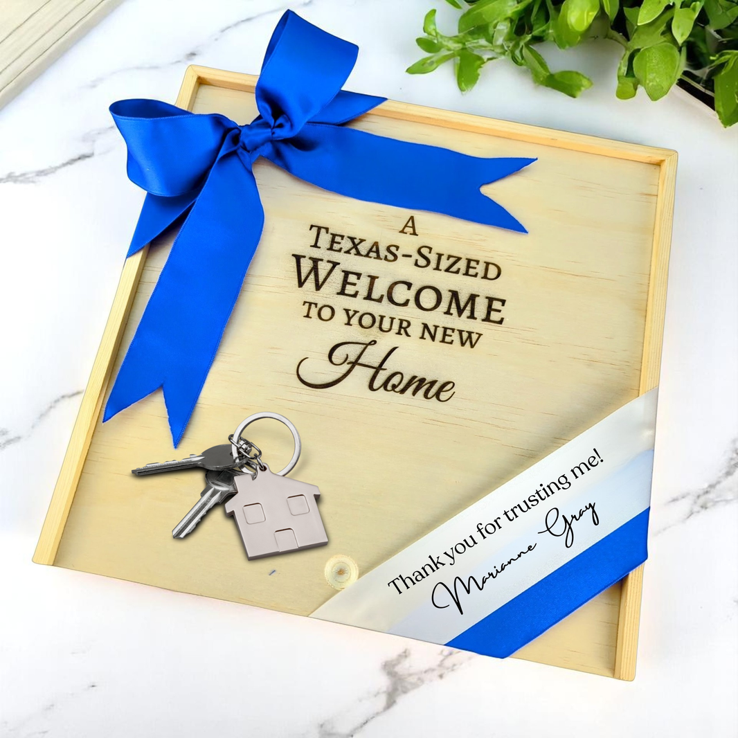 Wooden gift box with 'A Texas-Sized Welcome to Your New Home' text, keys, and blue ribbon on a marble surface