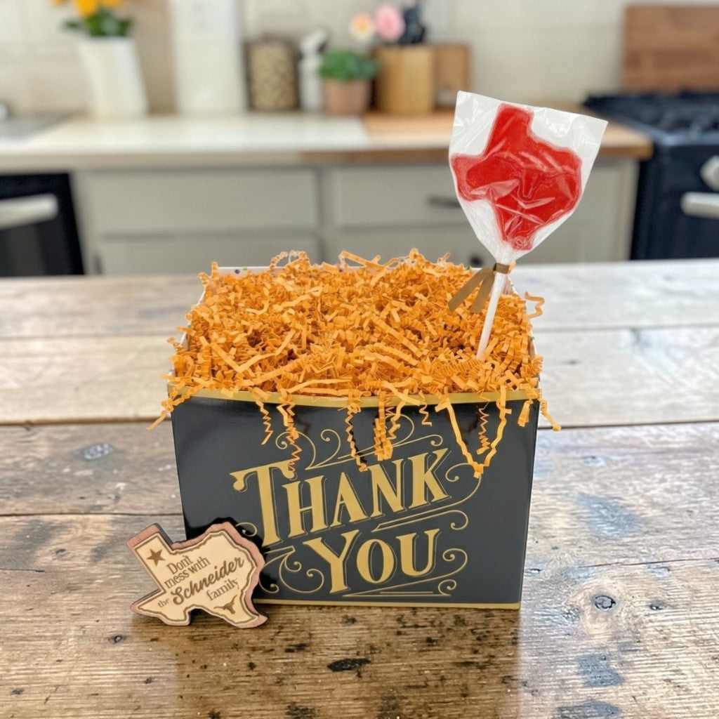 Box with 'Thank You' text, orange crinkle paper, and a lollipop on a wooden surface.