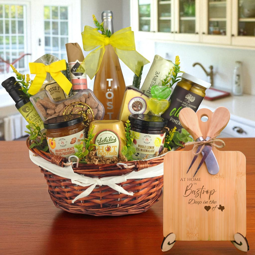 A gourmet gift basket paired with the At Home in Bastrop Charcuterie Board, featuring bamboo wood, rustic utensils, and engraved Texas design, perfect for celebrating Bastrop’s charm.