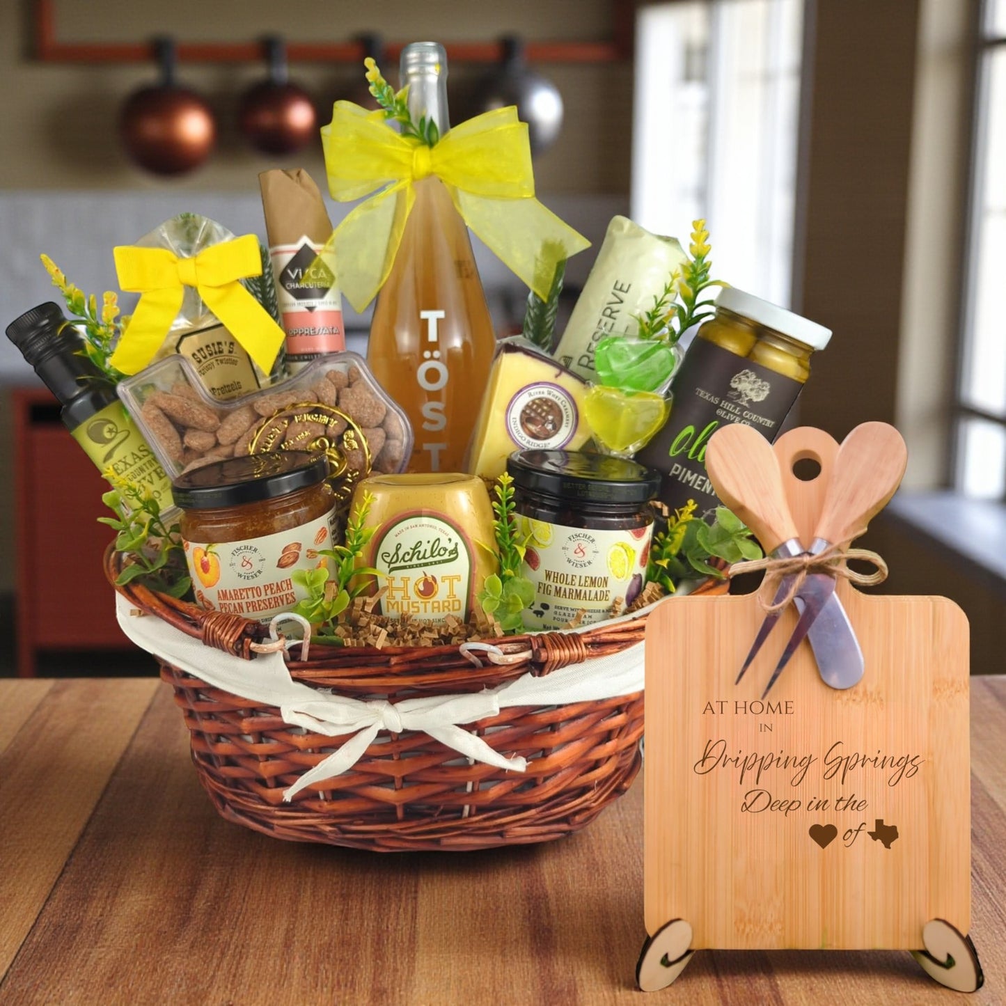 A gourmet gift basket paired with the At Home in Dripping Springs Charcuterie Board, featuring bamboo wood, rustic utensils, and engraved Texas design, perfect for celebrating Dripping Springs’ Hill Country charm.