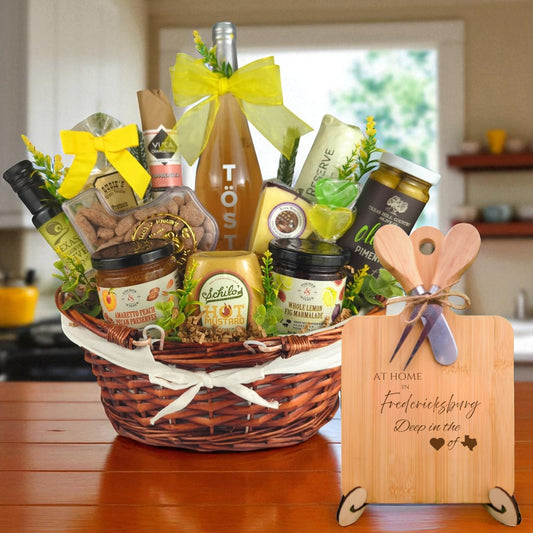 A gourmet gift basket paired with the At Home in Fredericksburg Charcuterie Board, featuring bamboo cutting board, rustic utensils, and engraved Texas design, perfect for celebrating Fredericksburg’s Hill Country charm.