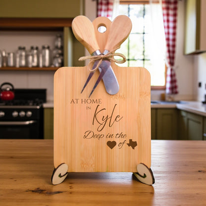 Bamboo charcuterie board engraved with “At Home in Kyle, Deep in the Heart of Texas” displayed on a kitchen counter with home décor in the background.