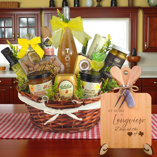 Gift basket filled with Texas treats, preserves, mustard, cheese, sparkling drink, and snacks, with a bamboo board engraved “At Home in Longview, Deep in the Heart of Texas” displayed in a kitchen.