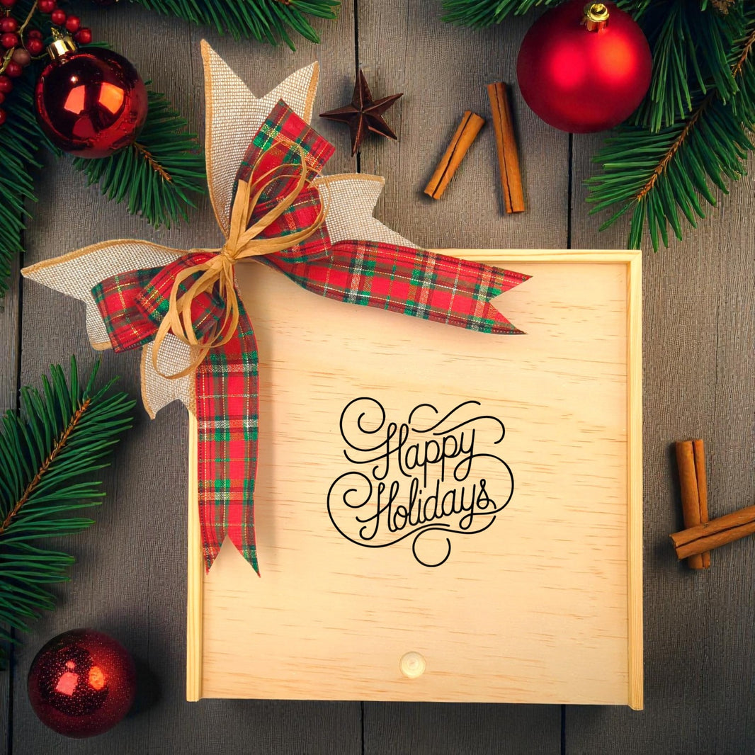 Create Your Own Happy Holidays Wooden Gift Box with a festive plaid ribbon and "Happy Holidays" design, surrounded by holiday greenery, cinnamon sticks, and seasonal decorations.