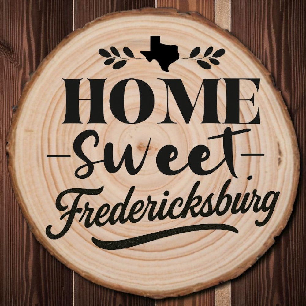 Rustic wood slice coaster with “Home Sweet Fredericksburg” laser engraving, Texas silhouette, and leafy accents on dark wood background