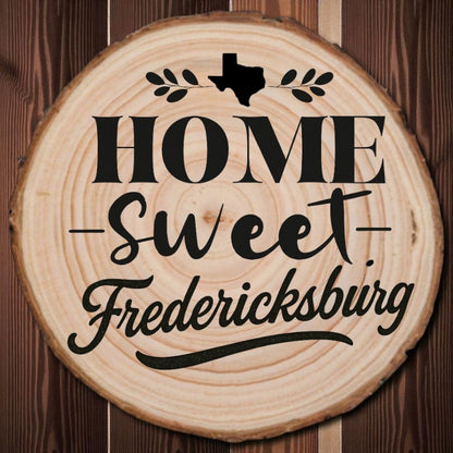 Rustic wood slice coaster with “Home Sweet Fredericksburg” laser engraving, Texas silhouette, and leafy accents on dark wood background
