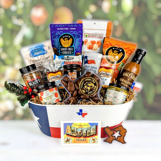 Austin-themed Texas gift basket from texasgiftbaskets.com, filled with pecans, maple pecan treats, gluten-free cookies, popcorn, BBQ sauce, peach jam, mustard, marmalade, yogurt pretzels, and sausage, presented in a Texas-flag-lined basket with an Austin greeting card.