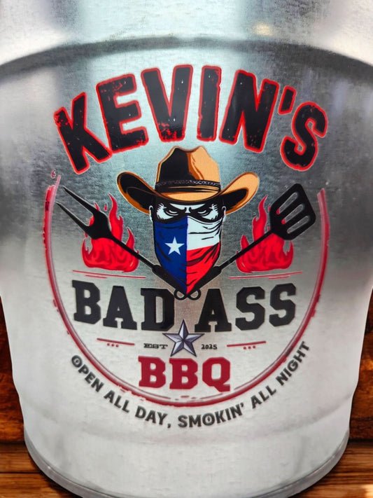 Close-up of BAD ASS BBQ Bucket showing engraved BAD ASS BBQ logo and personalized grill master’s name on a shiny galvanized steel surface.