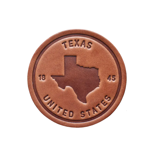 A round brown leather coaster with the embossed silhouette of Texas and the text 'Texas United States 1845'.