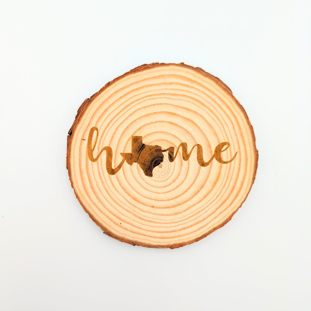 a wood slice coaster with engraving in cursive of the word home with the image of texas 