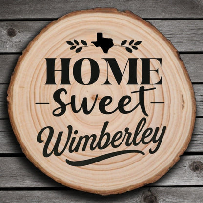 Rustic wood slice coaster with “Home Sweet Wimberley” laser engraving, Texas silhouette, and leafy accents on wood background.