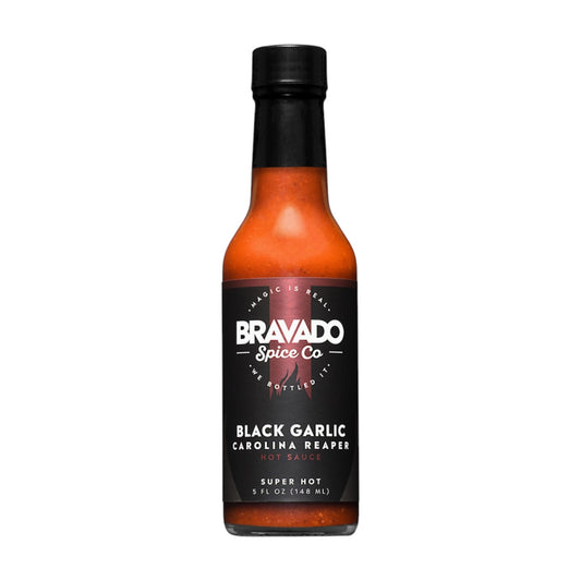 Bottle of Bravado Spice Co. Black Garlic Carolina Reaper hot sauce labeled “Super Hot,” containing a deep orange-red sauce in a clear glass bottle with a black cap, photographed on a white background