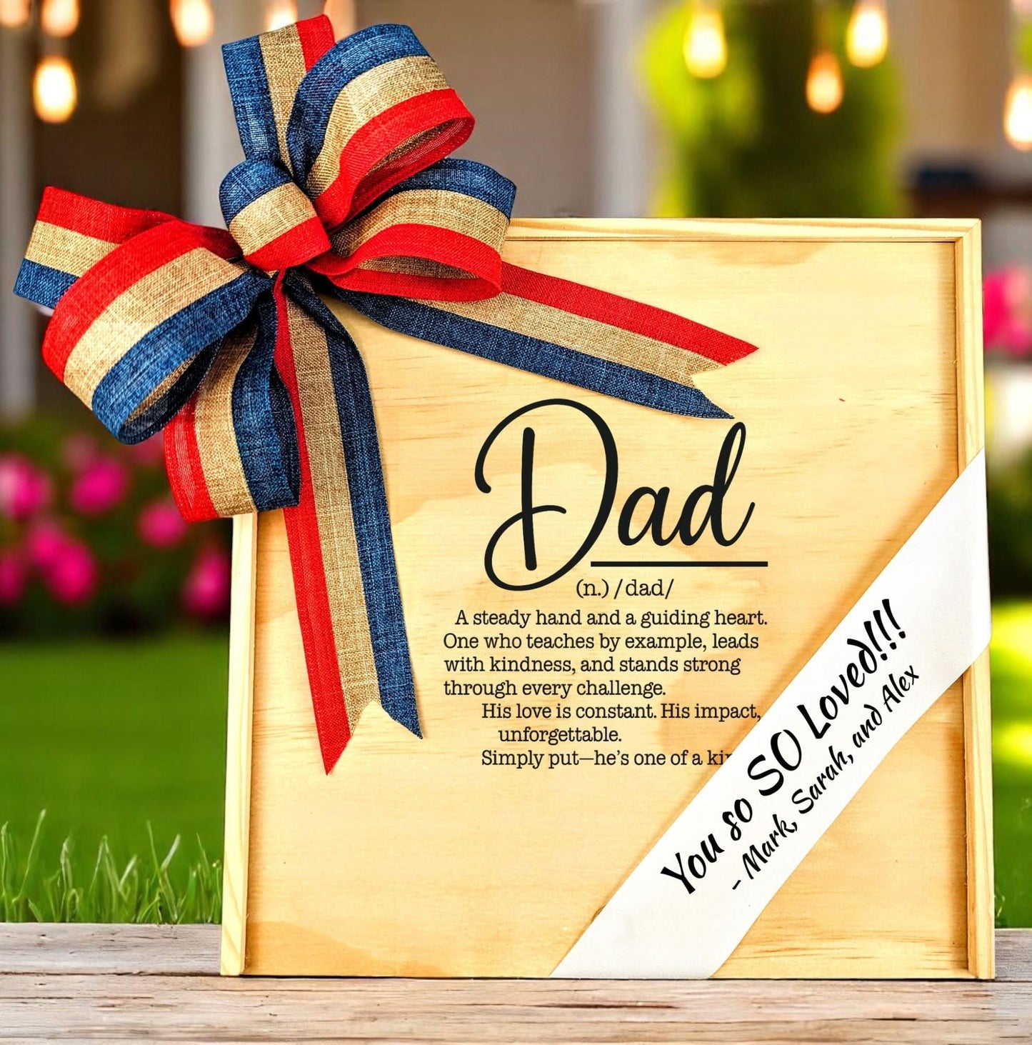 A wooden gift box featuring the 'definition of dad' text and a custom-printed ribbon on the lid, adorned with a red, white, and blue bow.