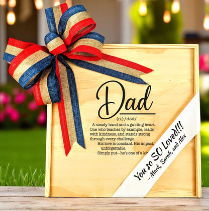 A wooden gift box featuring the 'definition of dad' text and a custom-printed ribbon on the lid, adorned with a red, white, and blue bow.
