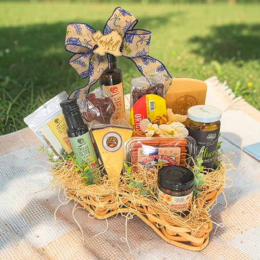 Hill Country Picnic gift in a Texas-shaped basket with cheese, sausage, crackers, balsamic vinegars, olives, preserves and a bamboo cutting board. Decorative styling shown.