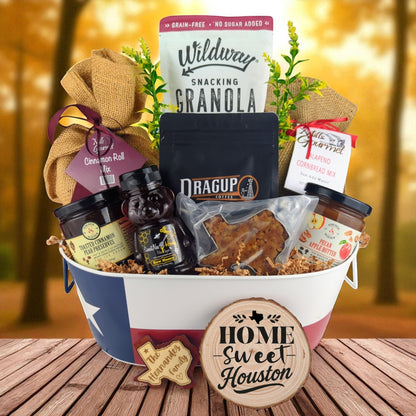 Houston Home Breakfast Basket with rustic background, Texas-themed tin filled with pecan coffee, cinnamon roll mix, jalapeño cornbread mix, granola, honey, praline, and preserves.