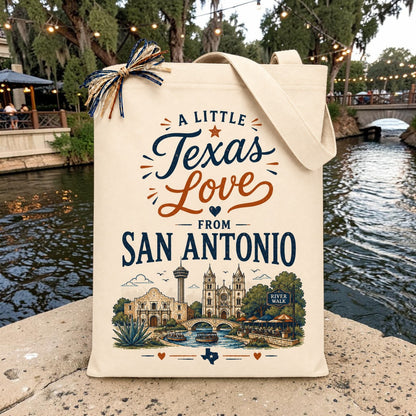 Natural canvas tote featuring the "A Little Texas Love from San Antonio" design with the Alamo, River Walk, Tower of the Americas, and San Fernando Cathedral, displayed along the San Antonio River Walk.