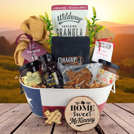 McKinney Breakfast Celebration Basket with rustic outdoor background, Texas-themed tin filled with pecan coffee, cinnamon roll mix, jalapeño cornbread mix, granola, honey, praline, and preserves.