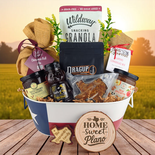 Plano Texas Breakfast Basket with rustic outdoor background, Texas-themed tin filled with pecan coffee, cinnamon roll mix, jalapeño cornbread mix, granola, honey, praline, and preserves.