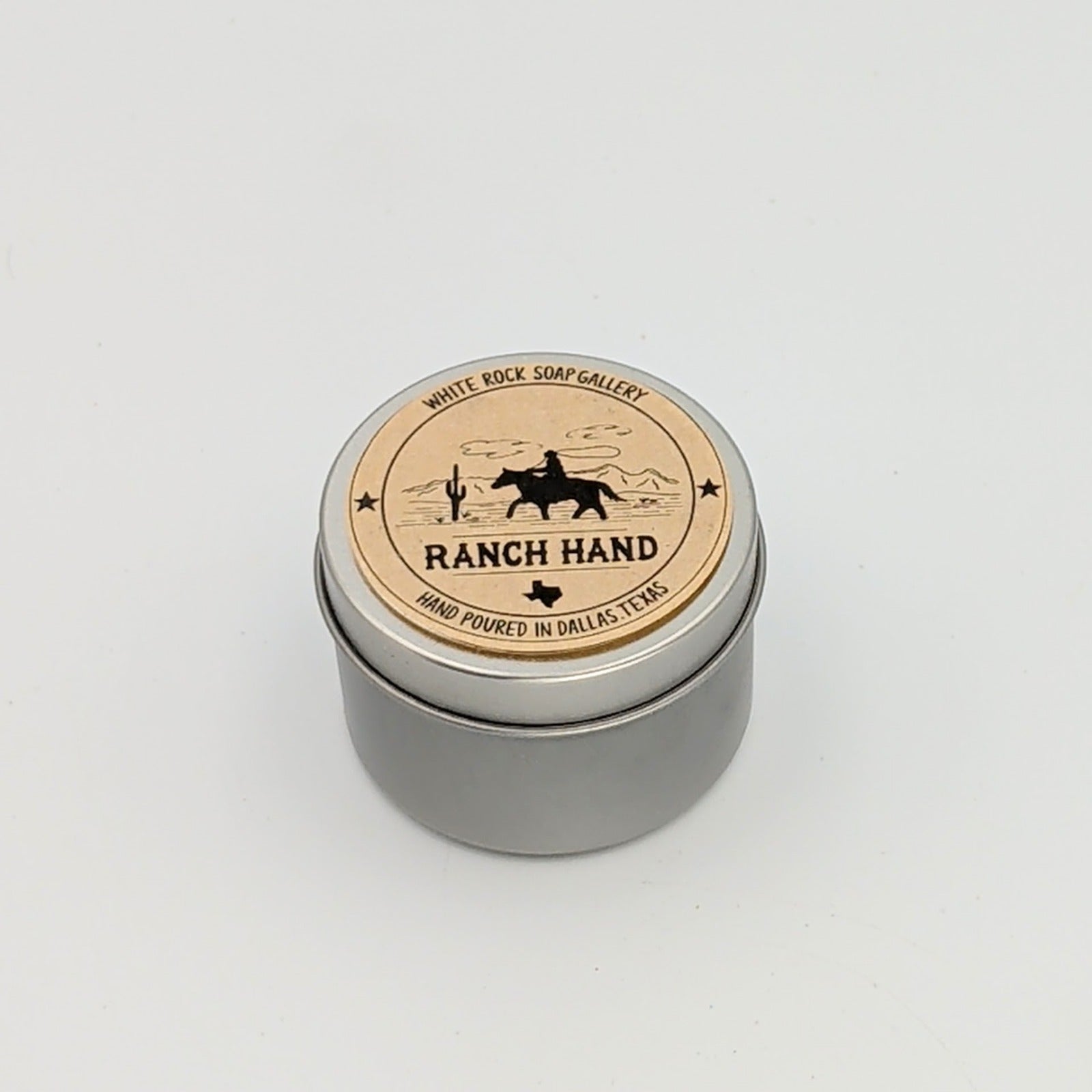 Silver metal candle tin labeled “Ranch Hand” with a silhouette of a cowboy on horseback and desert scenery, hand poured in Dallas, Texas, on a white background.