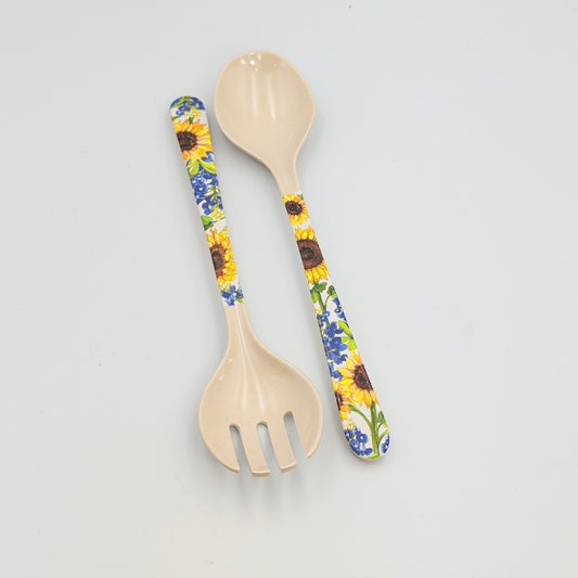 Two-piece salad server set featuring a spoon and slotted fork made of light-colored melamine with decorative handles printed with sunflowers and bluebonnets, arranged on a white background.