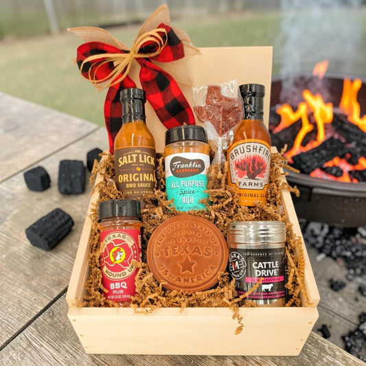 Texas Pitmaster Pantry wooden gift box with barbecue sauces, rubs, a Texas leather coaster and Texas-shaped lollipop beside a fire.
