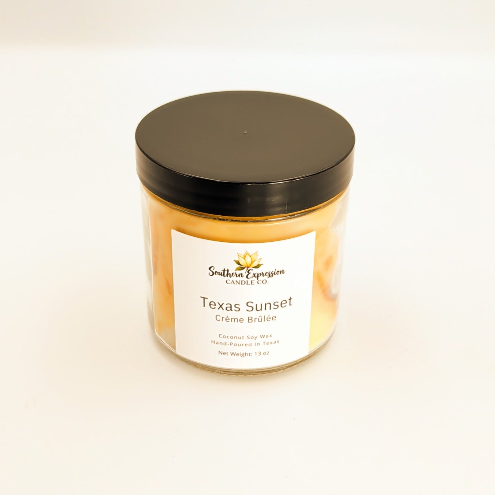 Amber-toned glass jar candle with black lid labeled “Texas Sunset – Crème Brûlée” by Southern Expression Candle Co., made with coconut soy wax and hand poured in Texas, photographed on a white background.