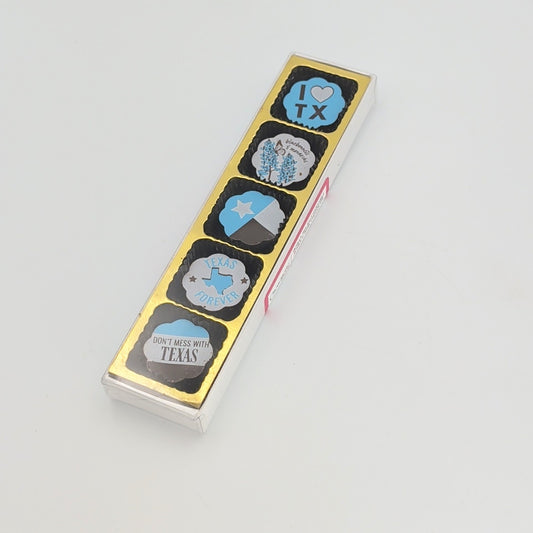 Slim rectangular clear gift box displaying five Texas-themed chocolate-covered caramels with designs including “I Love TX,” bluebonnets, the Texas flag, “Texas Forever,” and “Don’t Mess With Texas,” arranged on a gold backing against a white background.