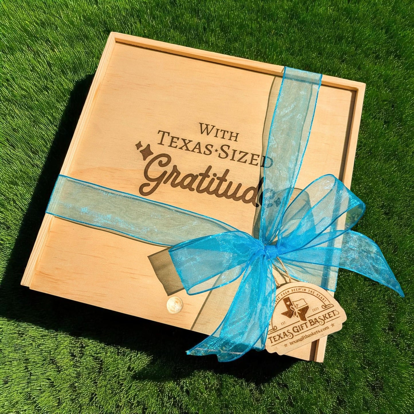 a wood gift box engraved with "With Texas-Sized Gratitude" on the lid, with a light blue ribbon and a Texas Gift Baskets tag 