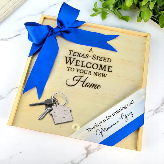 Wooden gift box with 'A Texas-Sized Welcome to Your New Home' text, keys, and blue ribbon on a marble surface