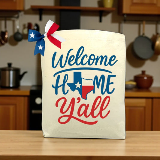 Canvas tote bag with the phrase “Welcome Home Y’all,” styled with a warm, welcoming design, perfect for filling with customizable Texas snacks and treats.